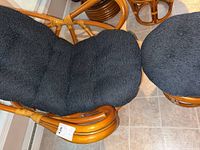 Rattan chair with black cushion on seat and backrest, showing curved natural brown rattan frame and wrapped rattan detailing on armrest.