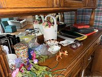 Serving dishes, ceramic canister, figurines, and assorted trays displayed on wooden furniture with plaid chair background