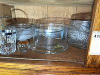 Shelf holding multiple pieces of glass and crystal serveware including bowls, an ice bucket, and a small jar with wooden lid.