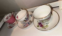 Photo showing four fine china teacups and saucers with floral patterns and gold trim.