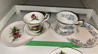 Two Royal Albert Bone China teacups with matching asymmetrical saucer plates displayed together, showing the floral pattern and gold detailing.