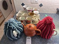 Photo showing all mugs on serving tray with two teapots and two knitted mug cozies