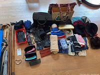 Wide shot of lot showing multiple women's accessories including hats, gloves, umbrellas, bags, walking canes, and scarves laid on a floor.