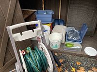 Overview of assorted yard supplies including garden hose on reel, buckets, plastic containers, and irrigation fittings set on gravel floor