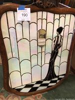 Full view of stained glass panel in wooden frame showing scalloped background, female figure and mirror insert