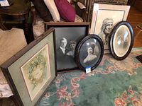 Overview of the six portraits including framed vintage photographs and colored artwork on floor in front of sofa.