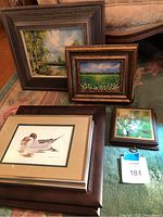 Photo showing the full group of seven framed artworks on a rug in front of a sofa, with close detail on frames and art.