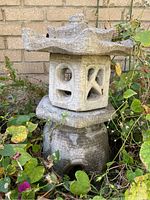 Side view of concrete pagoda lantern showing detailed top and base with surrounding foliage and brick wall background