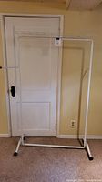 Full view of the white metal clothing rack showing base, vertical supports, horizontal hanging bar, and wire shelf.
