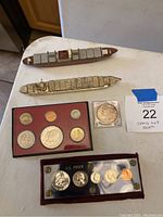 Overview of two metal ship figurines alongside coin sets