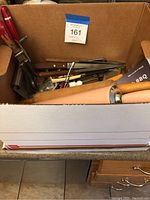 Top view of box filled with assorted cooking utensils including rolling pins and some knives visible
