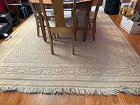 Full view of cream area rug under wood dining table on hardwood floor, showing fringed edge and textured pattern.