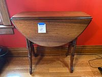 Front view of the wood drop leaf table with one leaf folded down, showing the table shape and surface.