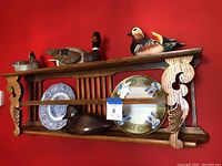 Front view of wooden wall shelf holding four carved and painted wooden ducks and two decorative display plates.