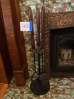 Fireplace tool set with wooden handles standing in metal holder next to a fireplace.
