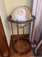 Full view of globe on wooden and brass stand, showing vintage globe mounted in circular wooden frame with brass rods.