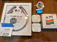 All items of the lot displayed including boxed LG wireless headphones, Apple iPod Shuffle with charging cable, two pairs of Apple wired earbuds in plastic cases, and boxed Bluetooth true wireless earbuds.