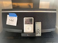 Klipsch black speaker system with silver control buttons on top, front mesh, vintage white iPod classic on dock, and Klipsch branded remote control to the right of iPod.