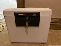 Beige rectangular SentrySafe locking file storage box with black lock panel and key inserted.