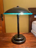 Side view of the lamp showing the black metal base and dome-shaped shade with glass disk above the base.