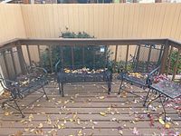 Full view of four-piece metal patio seating set on wooden deck with some fallen leaves. Includes loveseat, two chairs, small side table.