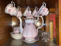 Royal Albert porcelain pink floral tea set displayed with six hanging teacups and stacked matching saucers, one cup handle broken