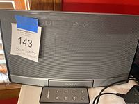 Front view of Bose speaker with metal grille and Bose remote control in front.