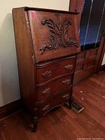 Full view of vintage wooden secretary desk with carved front panel and curved drawer fronts.