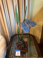 Front angle showing the stained glass blue butterfly with metal leaves and carved wood base on a glass table.