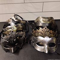 13 masquerade masks arranged in two piles showing style variety and design details in metallic colors with ribbon ties.