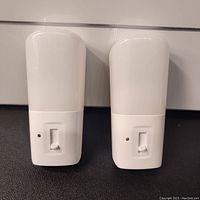 Two identical white immobile night lights with slider dimmer controls and small LEDs on front.
