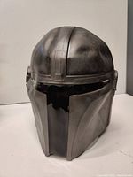 Front angled view of black rubber Mandalorian helmet mask showing ridges, matte surface, and black visor area.