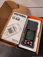 View of the moisture meter in packaging with user manual beside it.