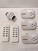 Overview of the lot items including three remote control outlet switches, one lamp socket adapter, and two remote controls arranged on a flat surface.