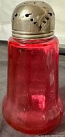 Front view of cranberry glass sugar shaker muffineer with silver plated top showing vent holes and rich red color.