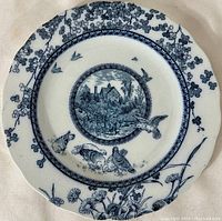 Full view of the blue and white dinner plate showing the floral rim and central rural scene with birds.