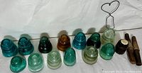 Full lot arranged in a line showing 13 glass insulators of various colors and sizes, plus 2 metal pieces and a heart-shaped wire holder.