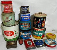 Wide view of collected vintage tins featuring tobacco, coffee, hand cleaner, honey, confectionery, and soap tins arranged on white background.