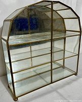 Front and right perspective view of brass and glass curio cabinet, showing frame and transparent panels.