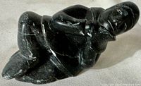 Black soapstone sculpture showing a reclining man holding a seal with visible details and some surface chips.