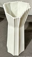 White bisque porcelain vase with vertical ribs, tapered hexagonal shape, and wavy rim viewed from front and sides.