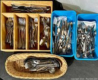 Multiple trays of assorted forks, spoons, and knives in stainless steel and silverplate in wooden and plastic compartments.