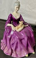 Front-left angle showing seated woman holding dog in purple dress with gold details.