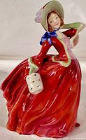 Front angled view of Royal Doulton Autumn Breezes figurine showing detailed red dress, blue scarf, and facial features.