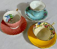 Photo showing three vintage Aynsley teacup and saucer sets: pink ribbed swirl, light blue with floral bouquets on corset cup, and yellow high-handled set.
