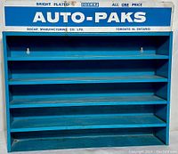 Front view of blue metal store display shelf with 'AUTO-PAKS' advertising on top panel and four shelves below.