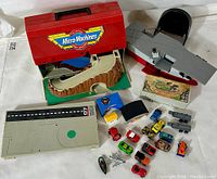 Overall view of the Micro Machines toy cars, playsets, and accessories including the red carrying case, aircraft carrier, and various vehicles arranged on a white surface.