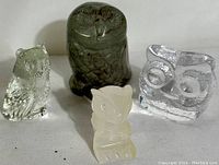 Four owl figurines on white background: clear textured glass, frosted stone, dark carved stone, clear smooth glass.
