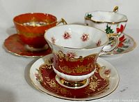 Three vintage teacup and saucer sets displayed with detailed patterns visible