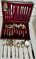 Full set of flatware displayed in open wooden chest showing various forks, spoons, knives and serving pieces.